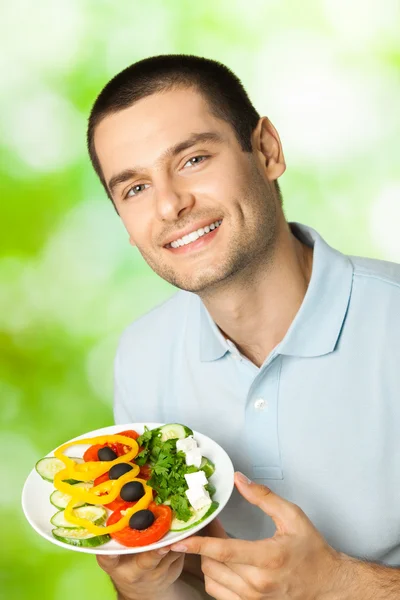 Porträt eines jungen glücklich lächelnden Mannes mit einem Teller Salat, im Freien — Stockfoto