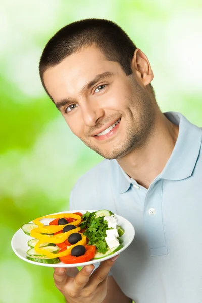 Portrait de jeune homme souriant heureux avec assiette de salade, extérieur — Photo