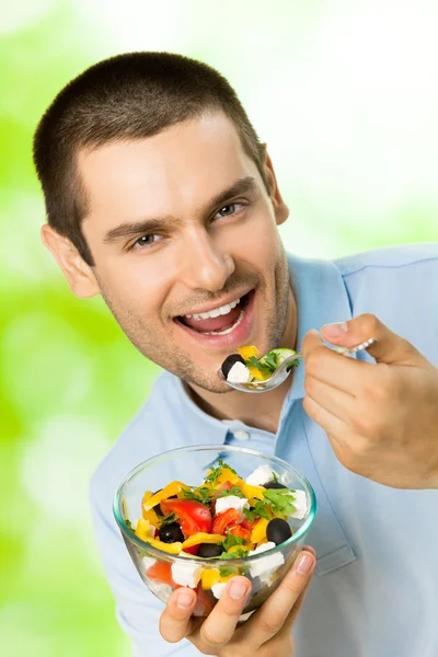Porträtt av ung glad man äta sallad, utomhus — Stockfoto