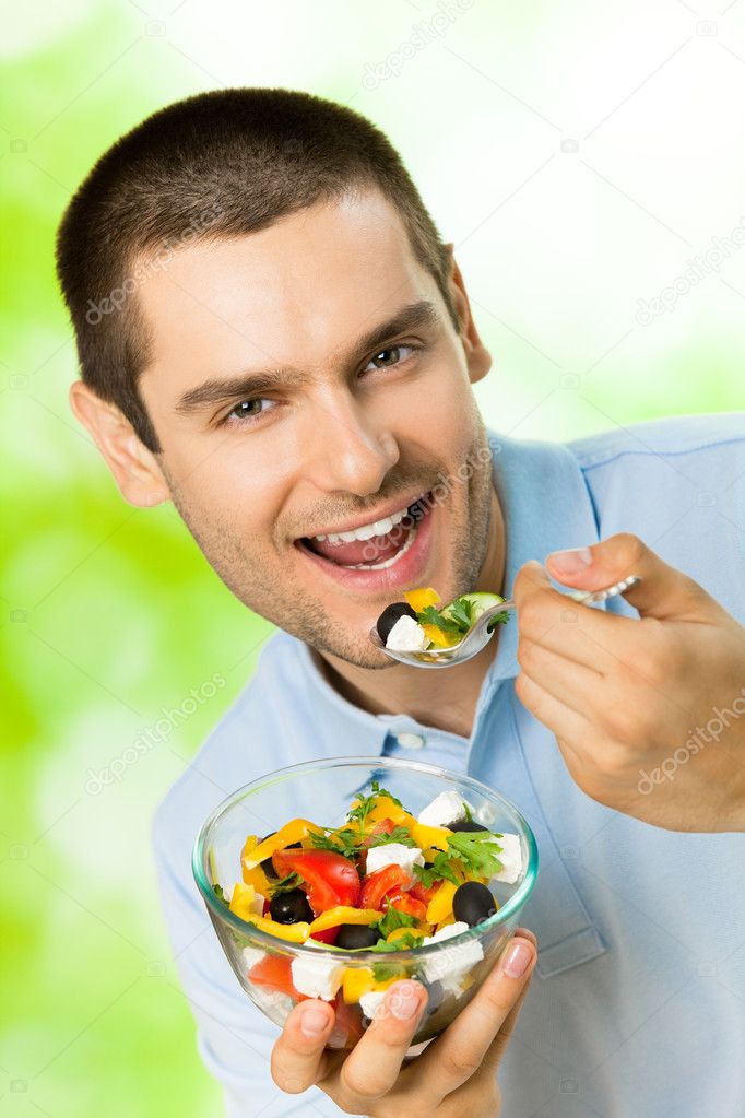 Portrait of young happy man eating salad, outdoors