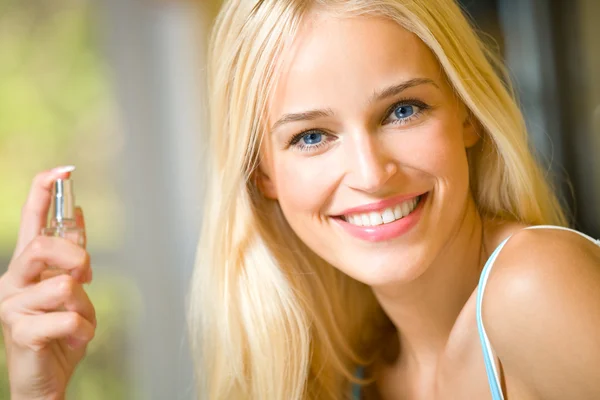 Молода щаслива усміхнена жінка з пляшкою парфумів у приміщенні — стокове фото
