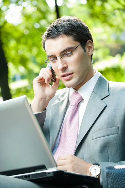 Hombre de negocios que trabaja con portátil y teléfono celular, al aire libre — Foto de Stock
