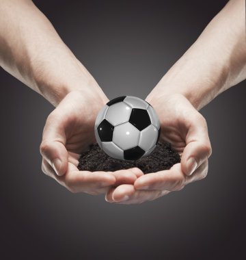 A handful soil with classic soccer ball in the man's hands clipart