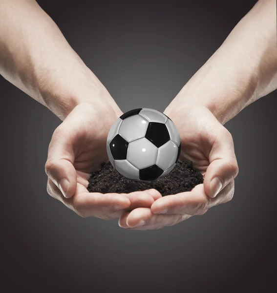 Eine Handvoll Erde mit klassischem Fußball in den Händen des Mannes — Stockfoto