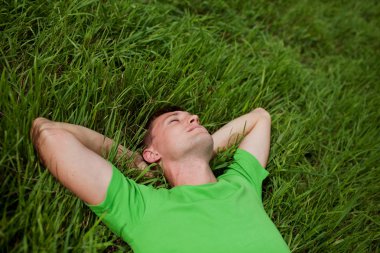 Genç adam çimlerin üzerinde yatıyor.