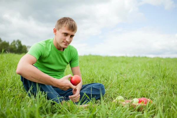 Ung man sitter på gräset med äpple — Stockfoto