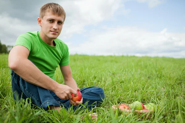 Apple ile çimlerde oturan genç adam — Stok fotoğraf