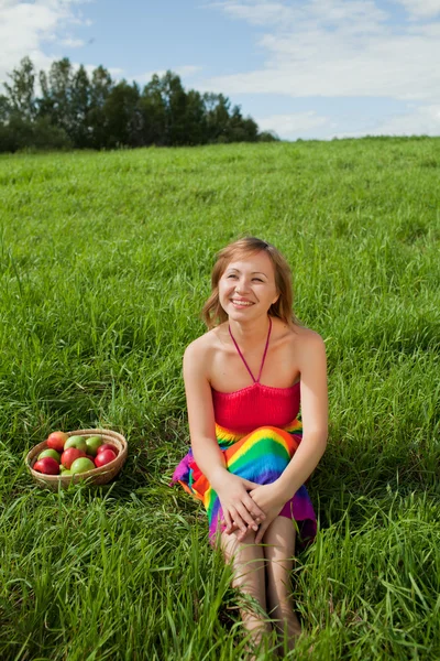 Menina na grama ao lado de uma cesta de maçãs — Fotografia de Stock