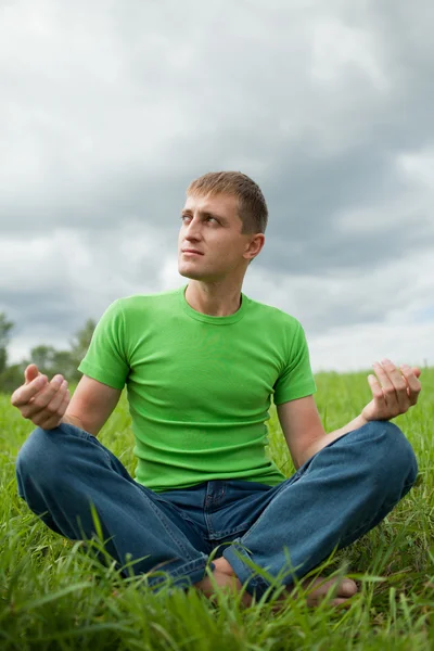 Молодой человек сидит на траве Стоковое Фото