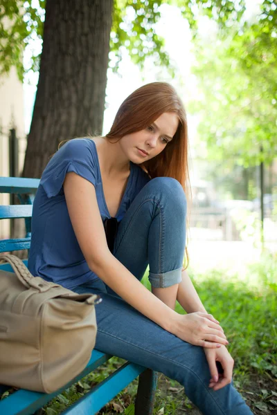 Sad girl sitting on a park bench — Stock Photo, Image