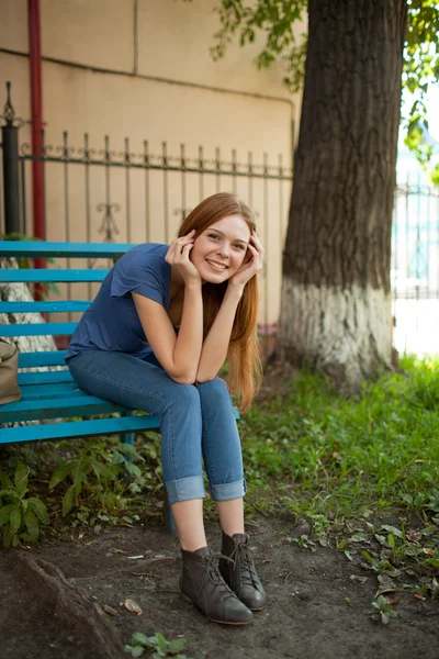 Улыбающаяся девушка сидит на скамейке в парке — стоковое фото