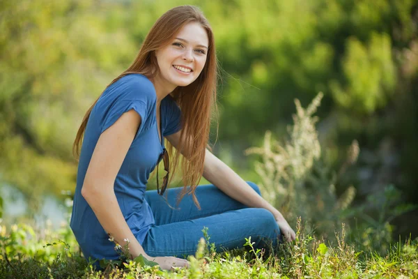 Красивая девушка сидит на траве и смотрит в камеру — стоковое фото