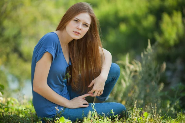 Menina bonita sentada na grama e olhando para a câmera — Fotografia de Stock