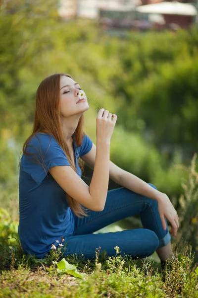 Девушка с маргаритками сидит на траве и нюхает ее. — стоковое фото