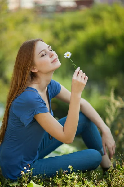 Dívka s sedmikrásky sedí v trávě a čichat — Stock fotografie