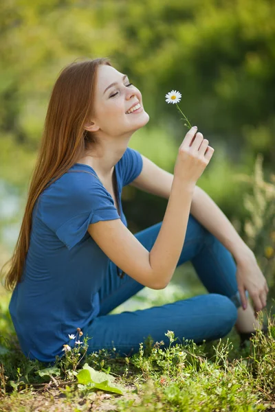 Dívka s sedmikrásky sedí v trávě a čichat — Stock fotografie