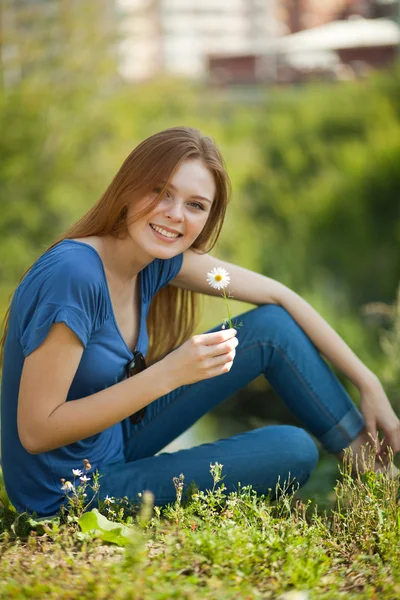 ผู้หญิงที่มีดอกเดซี่นั่งบนหญ้าและดมมัน — ภาพถ่ายสต็อก
