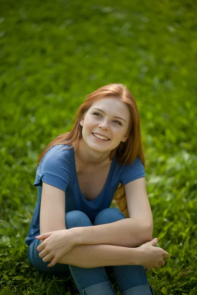 Gyönyörű vörös hajú lány ül a fűben — Stock Fotó