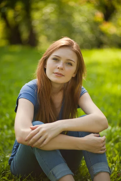 Schöne rothaarige Mädchen sitzt auf Gras — Stockfoto