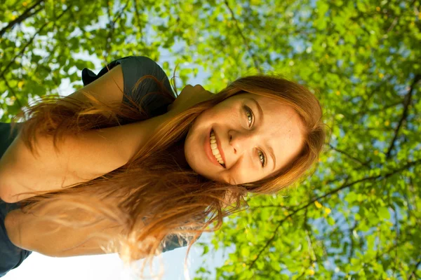 Gyönyörű vörös hajú mosolygó lány, a háttérben a lombozat — Stock Fotó