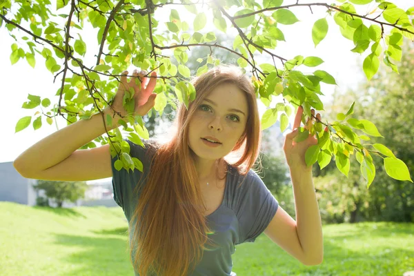 Vacker rödhårig leende flicka på en bakgrund av bladverk Stockfoto