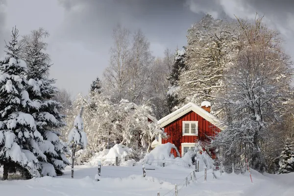 Röd stuga i snöiga landskap Stockbild