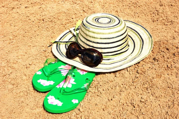 Zon hoed, zonnebril en slippers op het zand — Stockfoto