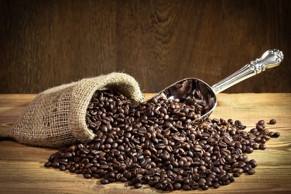 Kávová zrna na pytli s kovová naběračka na staré prkno — Stock fotografie