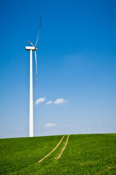 Turbina de viento con camino en campo verde con cielo azul —  Fotos de Stock