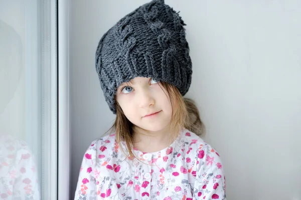 Adorable niña en sombrero de punto gris oscuro cerca de la ventana —  Fotos de Stock