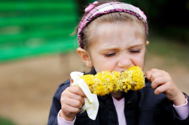 Pretty child girl eating a boiled corn outdoors clipart