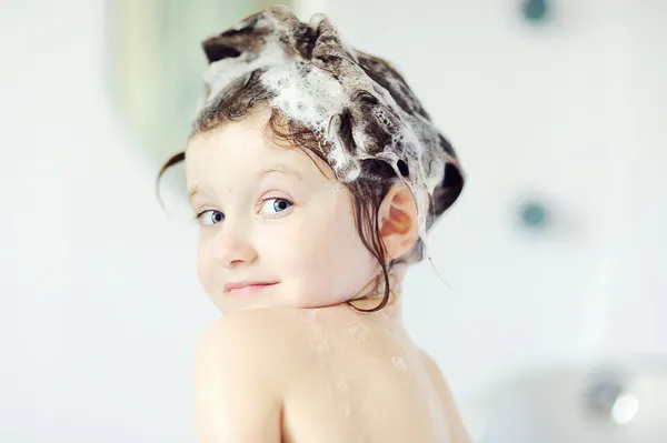 Barn flicka med schampo på hennes hår ser tillbaka i badkar — Stockfoto