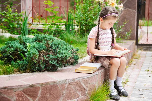 Молодая девушка с рюкзаком читает в ожидании школы — стоковое фото