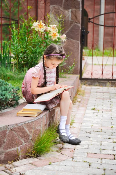 Chica joven con mochila lee esperando a la escuela — Foto de Stock
