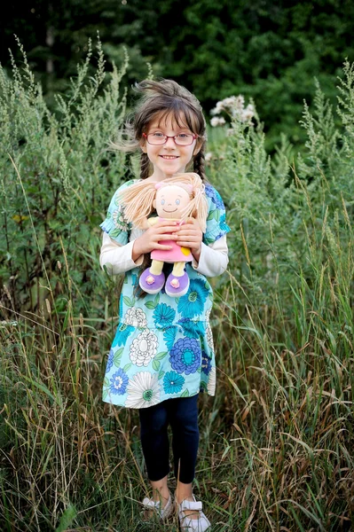 Adorable brunette kind meisje in blauwe zomerjurk hugs baby doll — Stockfoto