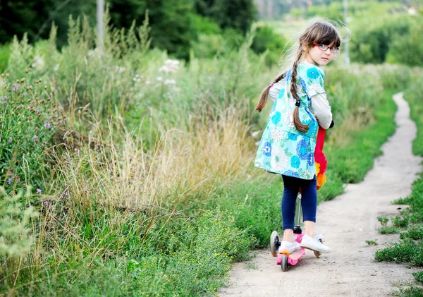 Roztomilé dítě dívka se ohlíží zpět při jízdě venku jí červená koloběžka — Stock fotografie