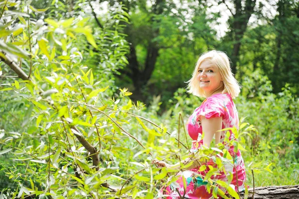 Entzückende blonde Frau sitzt auf einem Baumstamm im Wald — Stockfoto