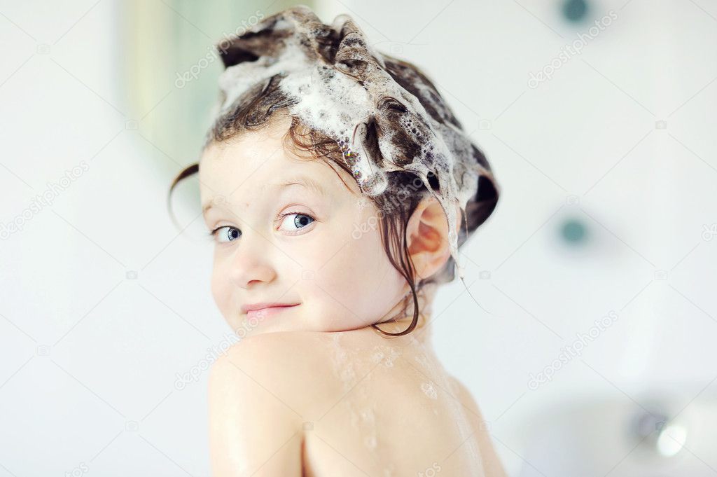 Child girl with shampoo on her hair looks back in bathtub