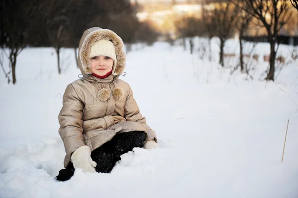 Child girl in winter coat with hood plays outdoors in snowfall — Stock Photo, Image