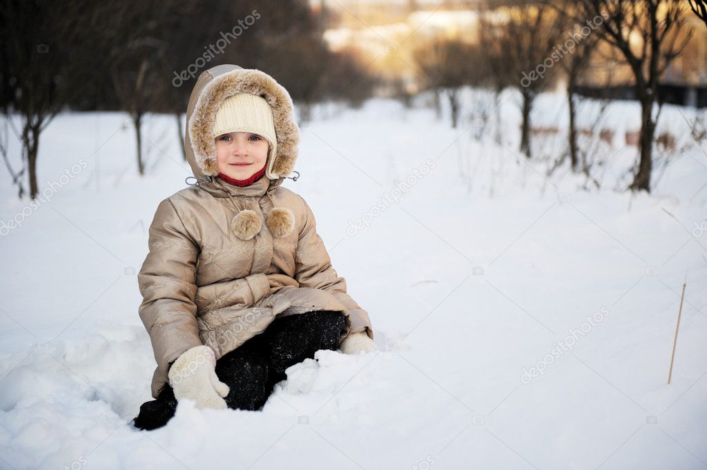 Child girl in winter coat with hood plays outdoors in snowfall
