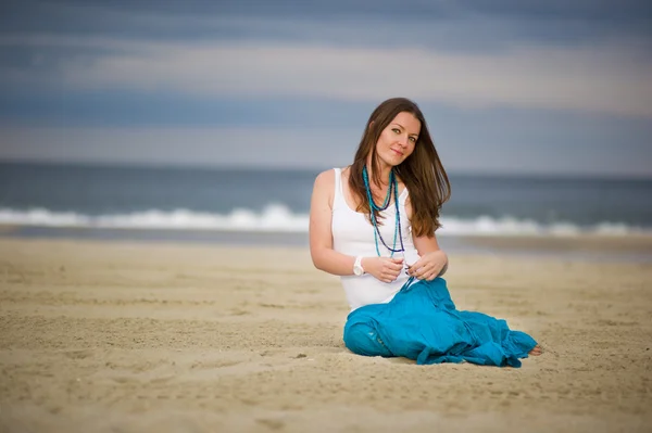 Krásná mladá žena sedí na písku v blízkosti oceánu — Stock fotografie