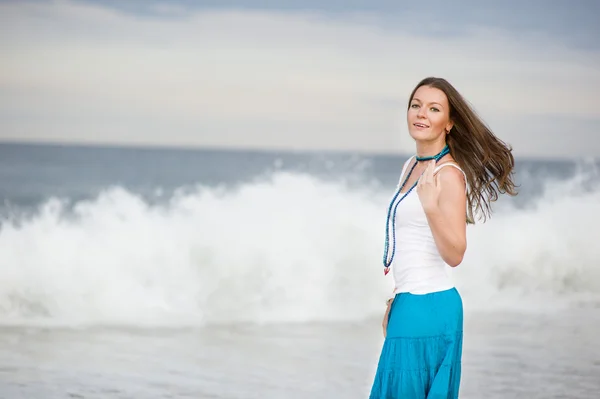 stock image Beautiful young woman stands against the ocean