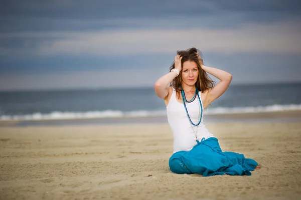 stock image Beautiful young woman sits on sand near the ocean