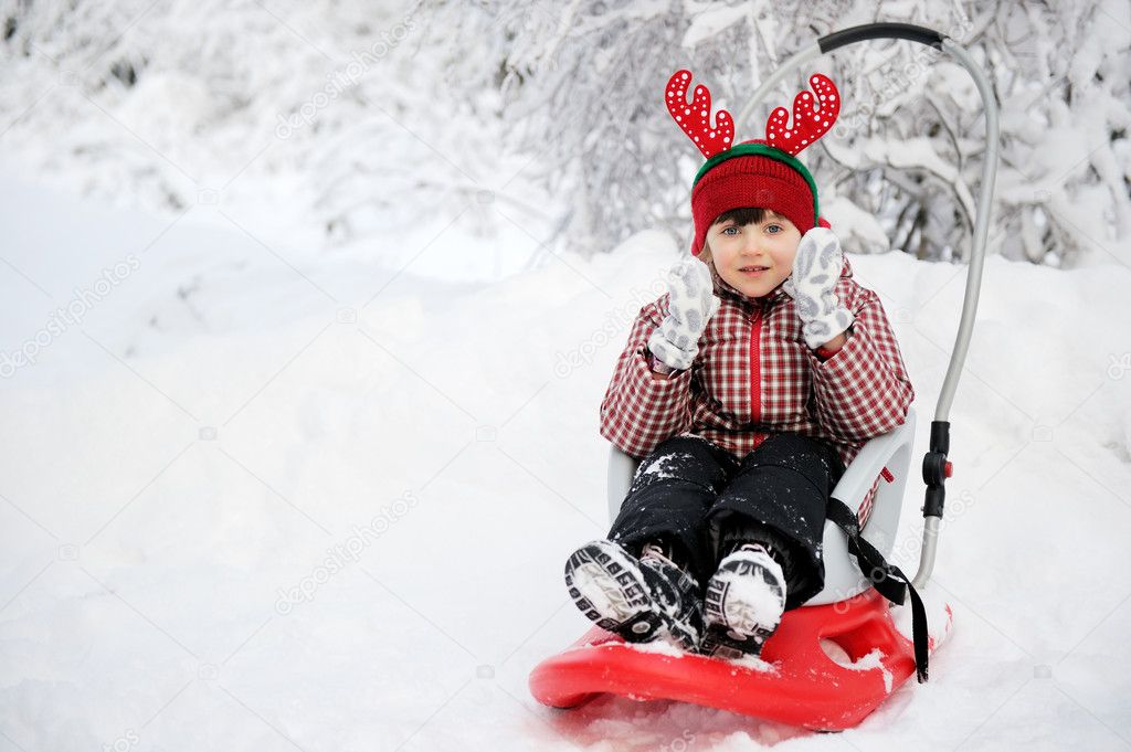 Adorable child girl in horned hat sled in snow