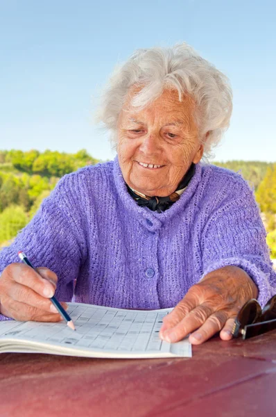 Starszy kobieta robi krzyżówka — Zdjęcie stockowe