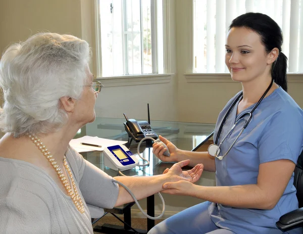 Enfermera joven midiendo la presión arterial del paciente — Foto de Stock
