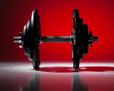 Single dumbbell dramatically lit on graduated red background.