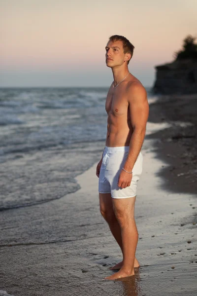 Aantrekkelijke man in ondergoed op een strand bij zonsopgang. — Stockfoto