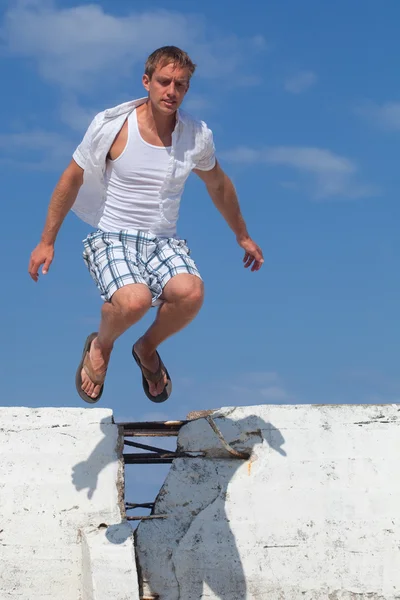 Een jonge man springen over een muur buiten. — Stockfoto