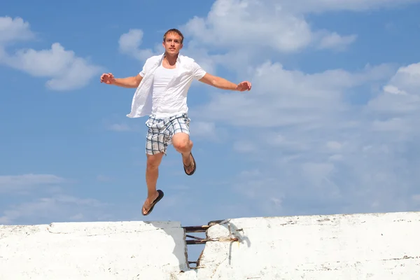 stock image A young man leaping over a wall outside.